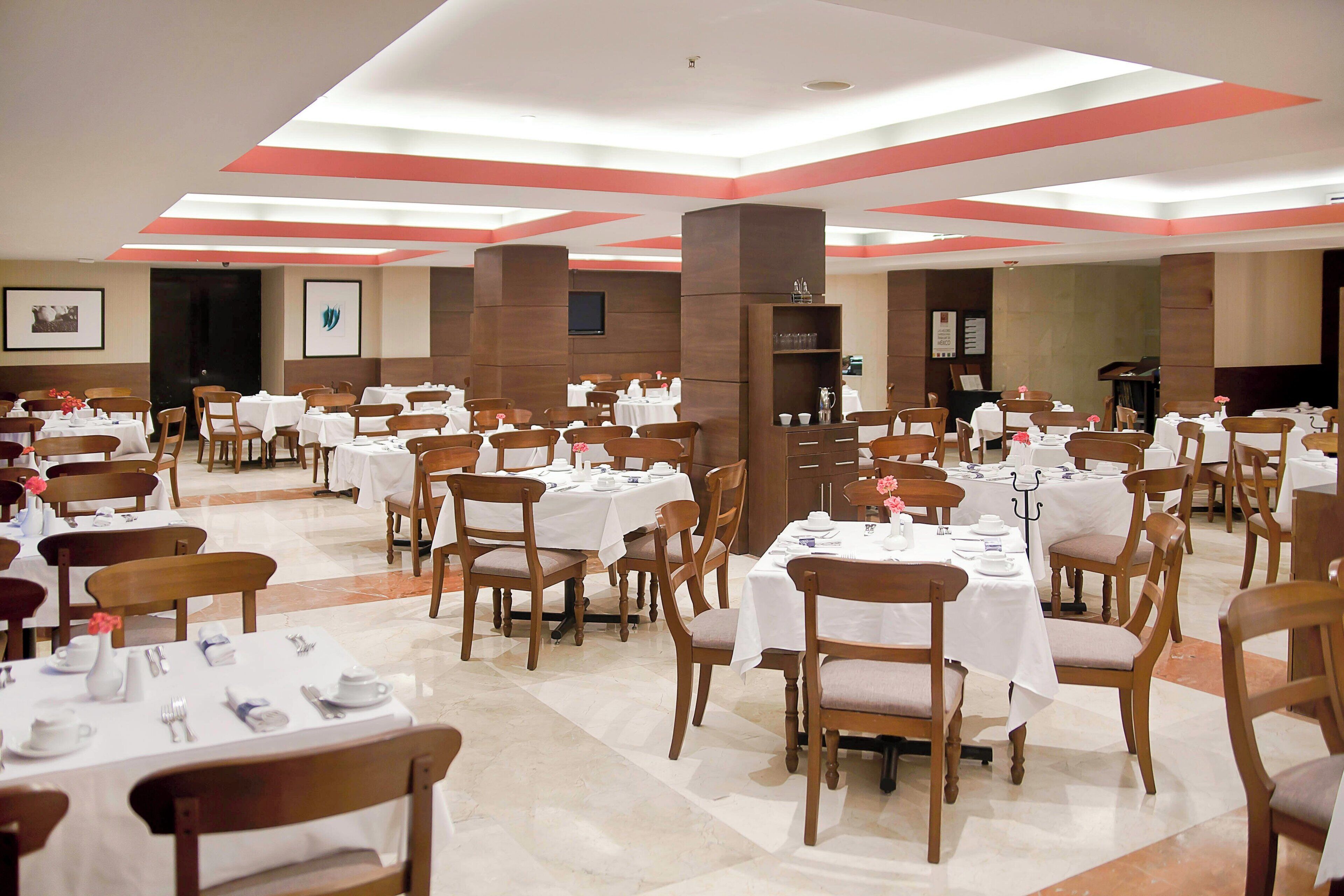Un amplio salón de banquetes con varias mesas redondas y sillas de madera, dispuestas en filas.
