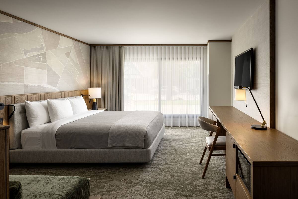 A hotel room with a large bed, a desk, a chair, a TV, and a window with curtains.