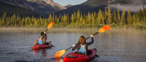 Two people kayaking on a calm lake with mountains in the background.