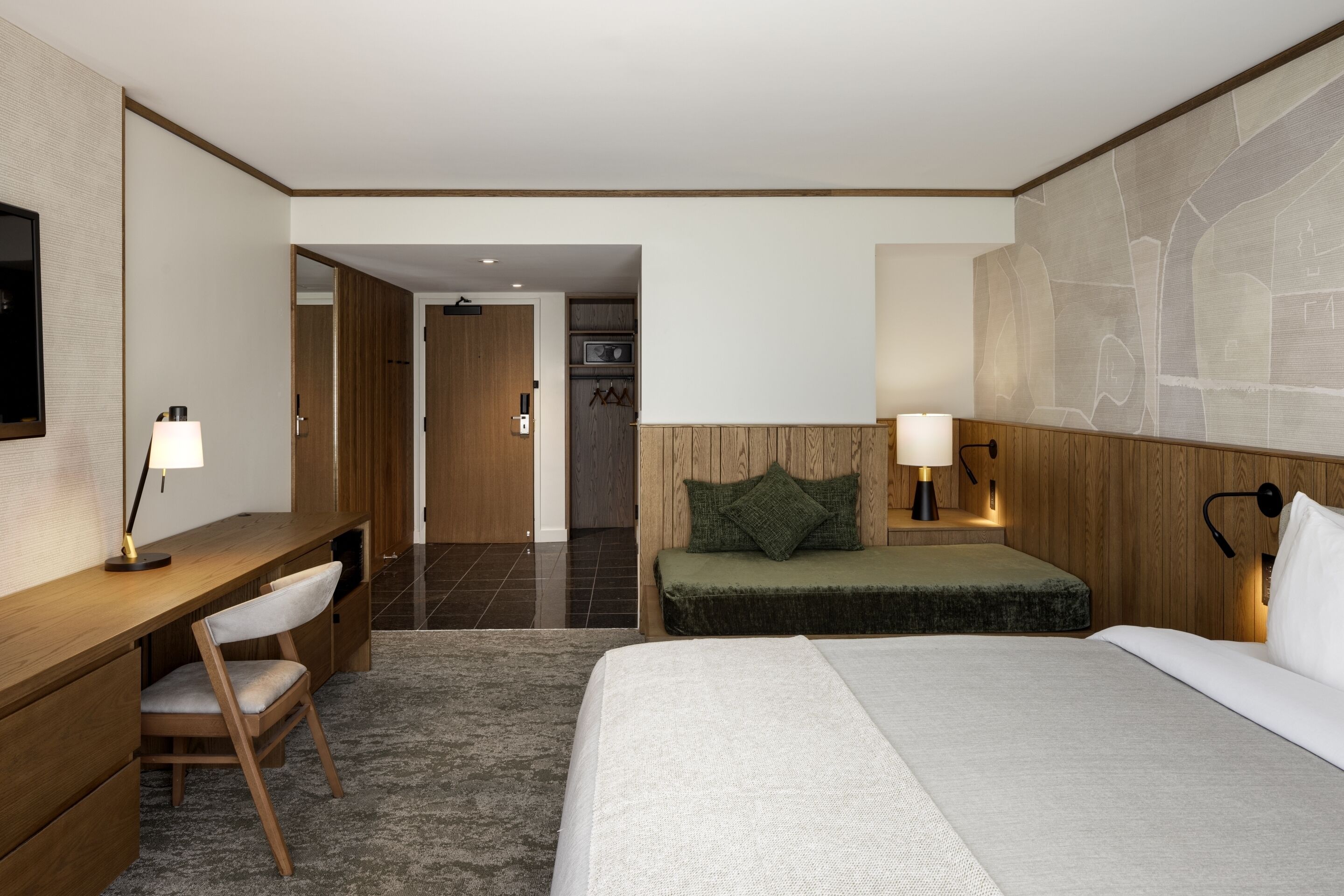 Une chambre d’hôtel équipée d’un lit, d’un bureau, d’une chaise, d’une table de chevet et d’une lampe fixée au mur.