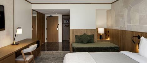 Une chambre d’hôtel équipée d’un lit, d’un bureau, d’une chaise, d’une table de chevet et d’une lampe fixée au mur.