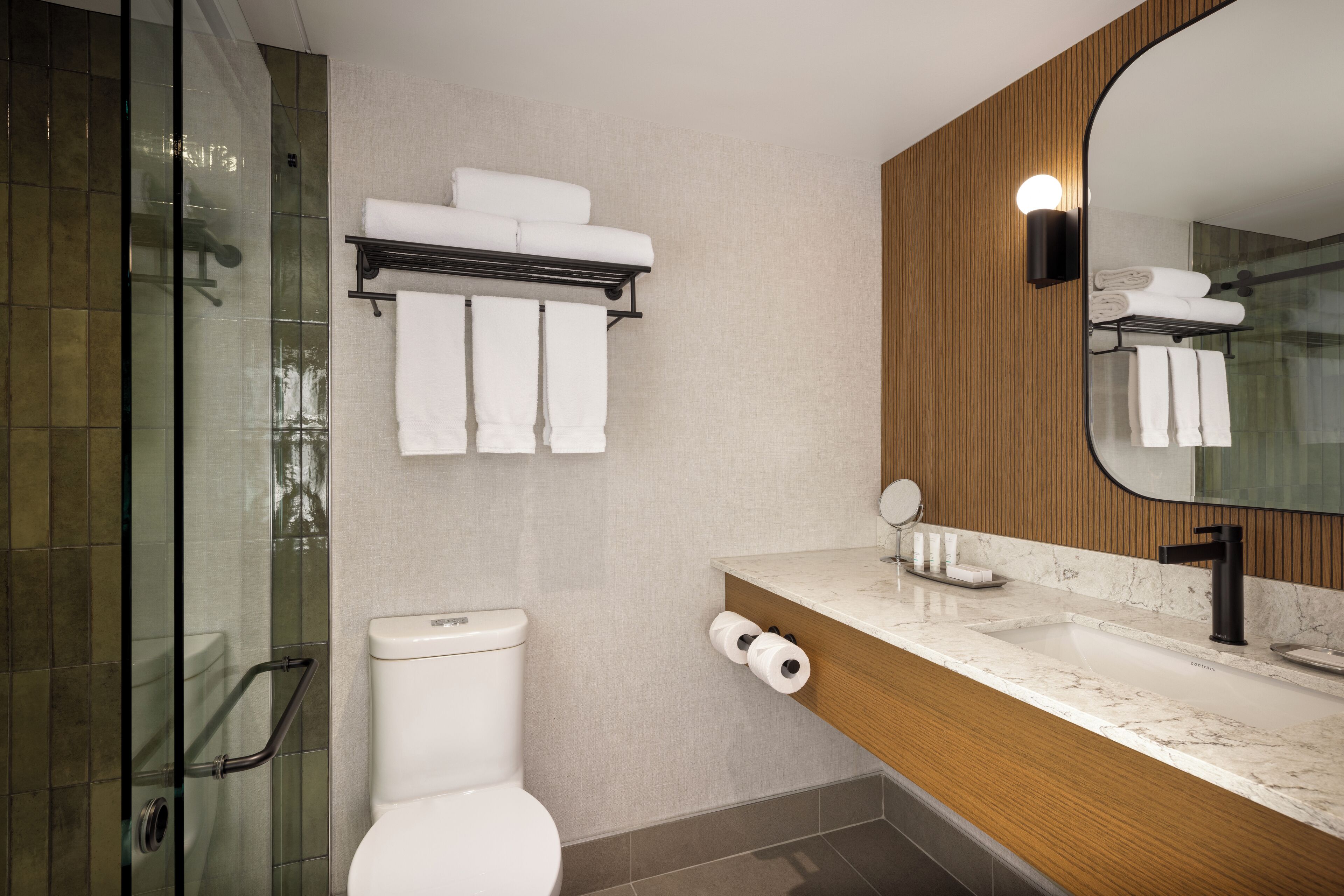 A modern bathroom with a glass shower enclosure, a toilet, a marble sink, and a wooden vanity.