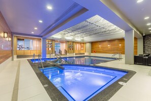 A modern indoor swimming pool with clear water, a sunroof, and a wooden wall on one side. - Banff Park Lodge (Banff)
