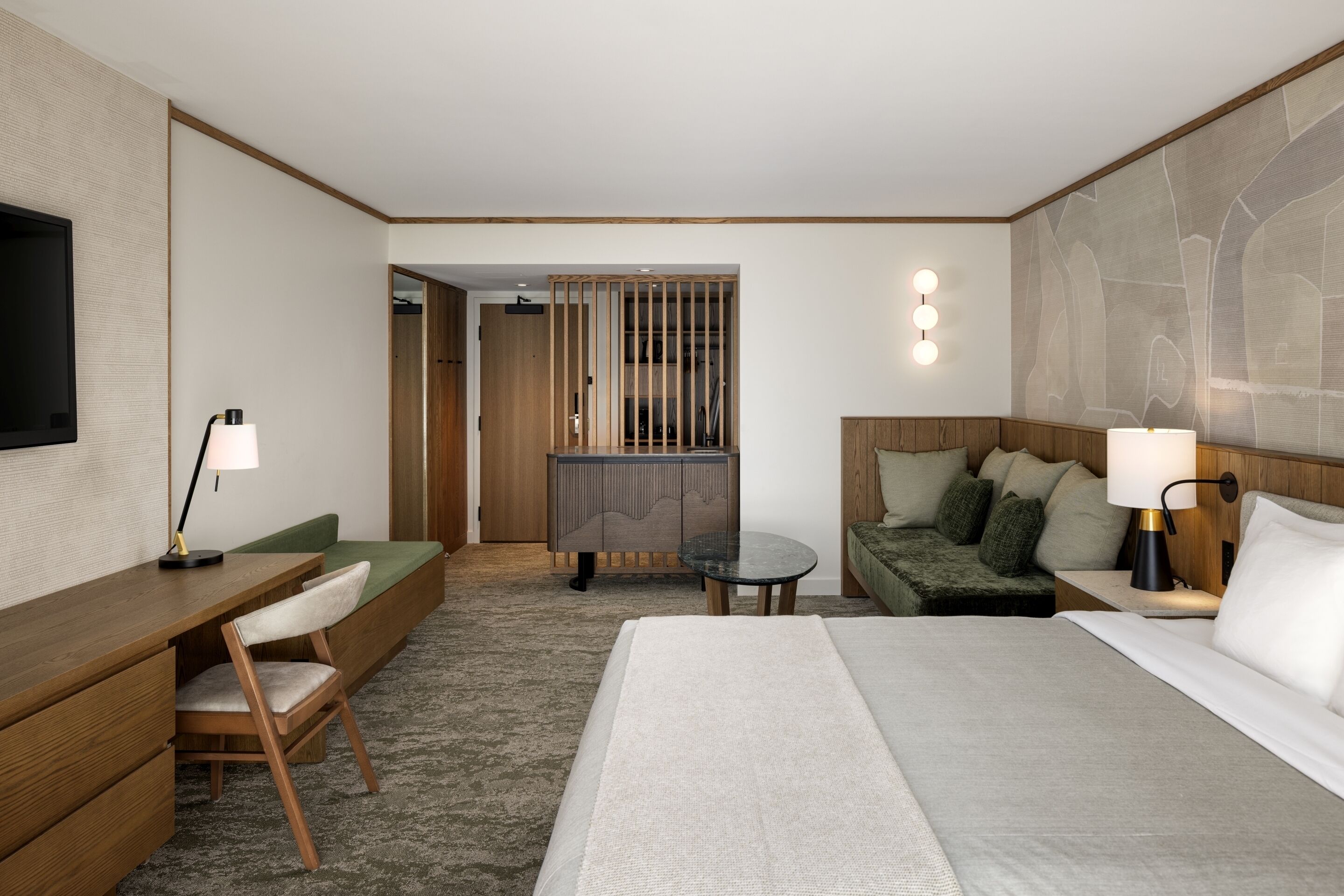 Una habitación de hotel con cama, escritorio y silla, una mesita, un sofá y televisor.