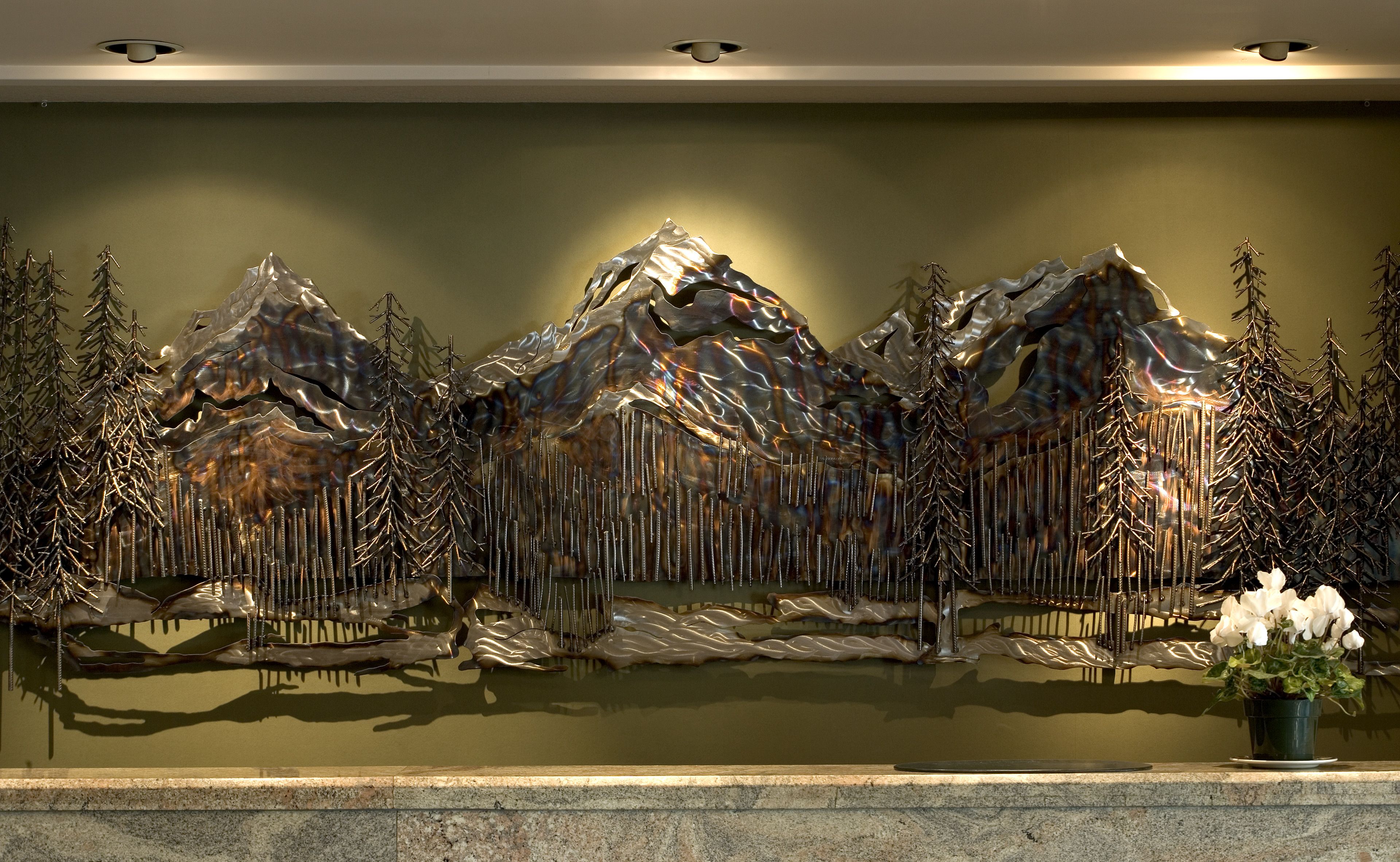 A wall-mounted sculpture of mountains with trees, a small potted plant, and a reflective surface below.