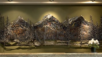 A wall-mounted sculpture of mountains with trees, a small potted plant, and a reflective surface below.
