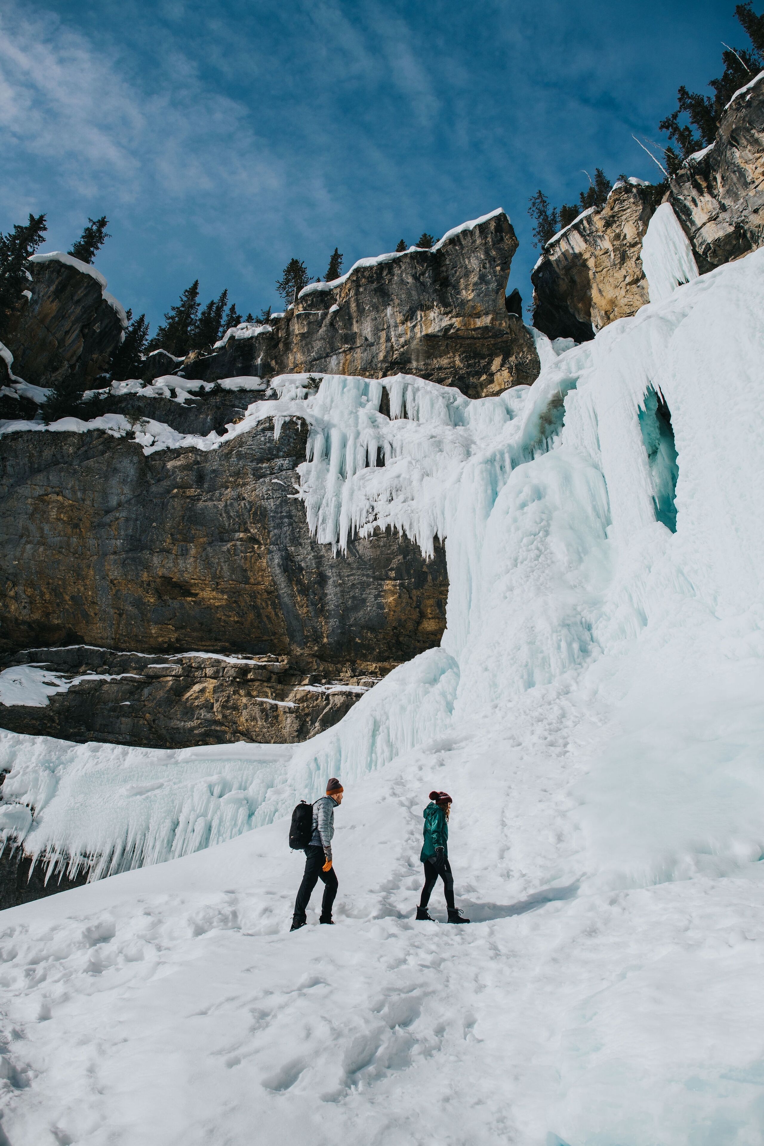 A snowy landscape with a large ice formation and two people standing on a snow-covered slope.