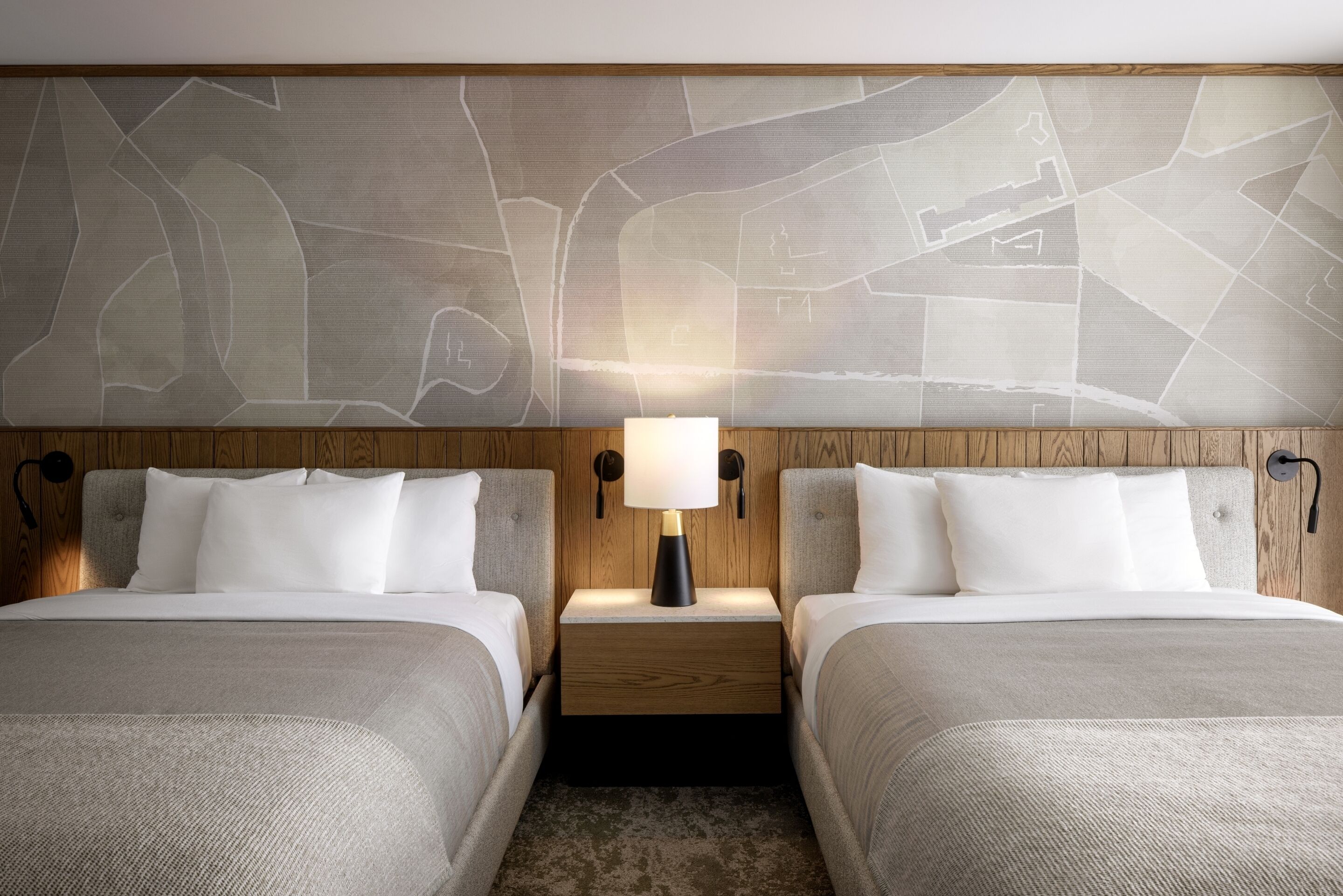 Een hotelkamer met twee bedden, een nachtkastje met een lamp en een grote abstracte wereldkaart aan de muur.