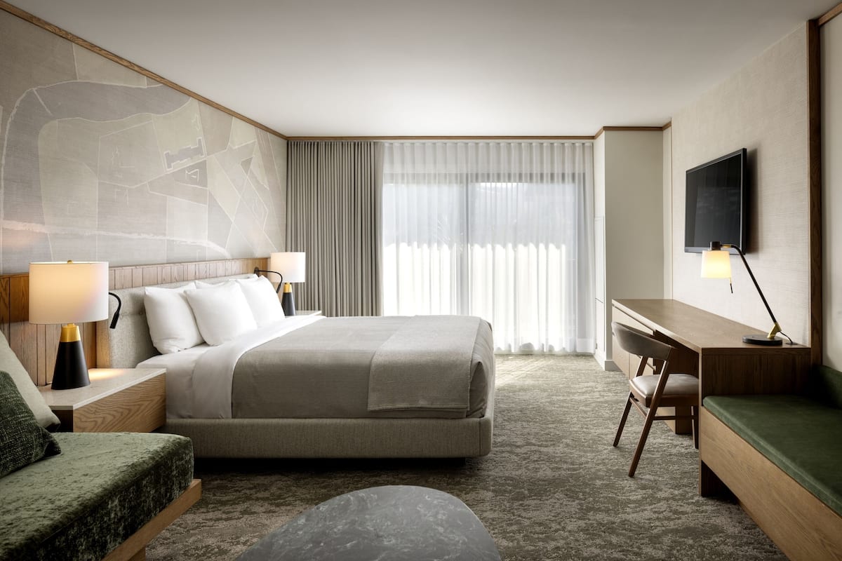 A hotel room with a large bed, a desk, a chair, a TV, and a map on the wall.