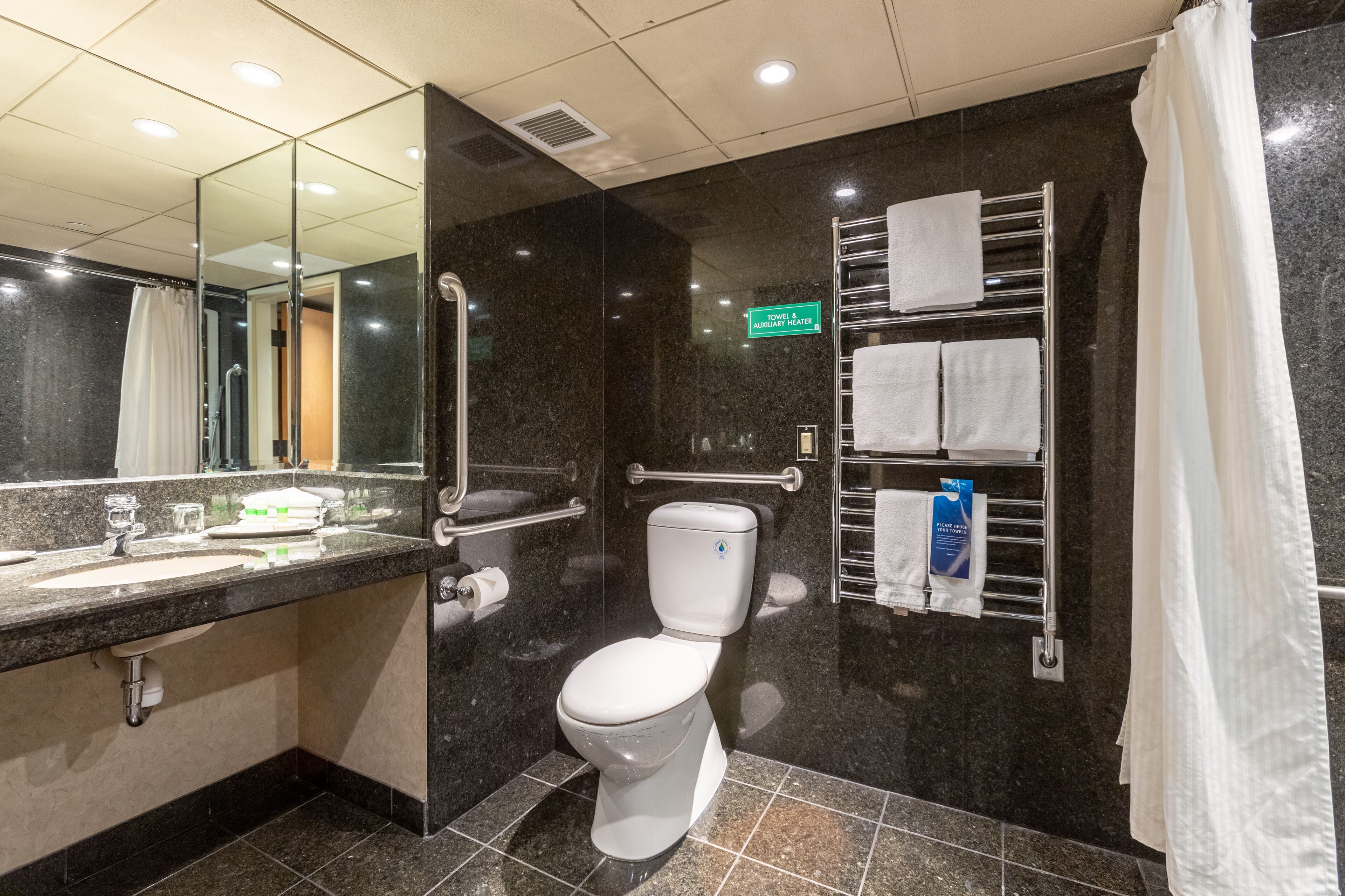 Un baño moderno con inodoro blanco, ducha con mampara de vidrio, tocador con espejo y un perchero para toallas.