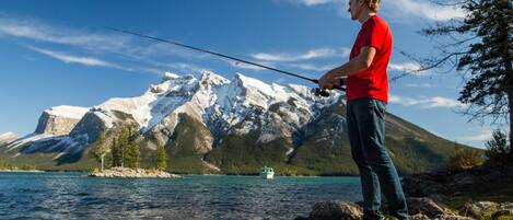 A person fishing by a lake with mountains in the background.