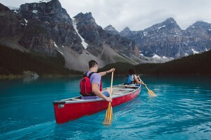 Un canoa rojo en un lago tranquilo con montañas al fondo.