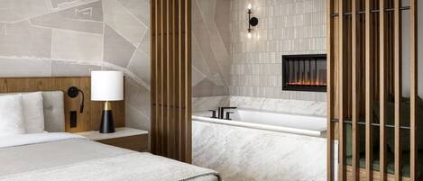 Una habitación de hotel moderna con una cama grande, un baño separado con bañera y una chimenea.
