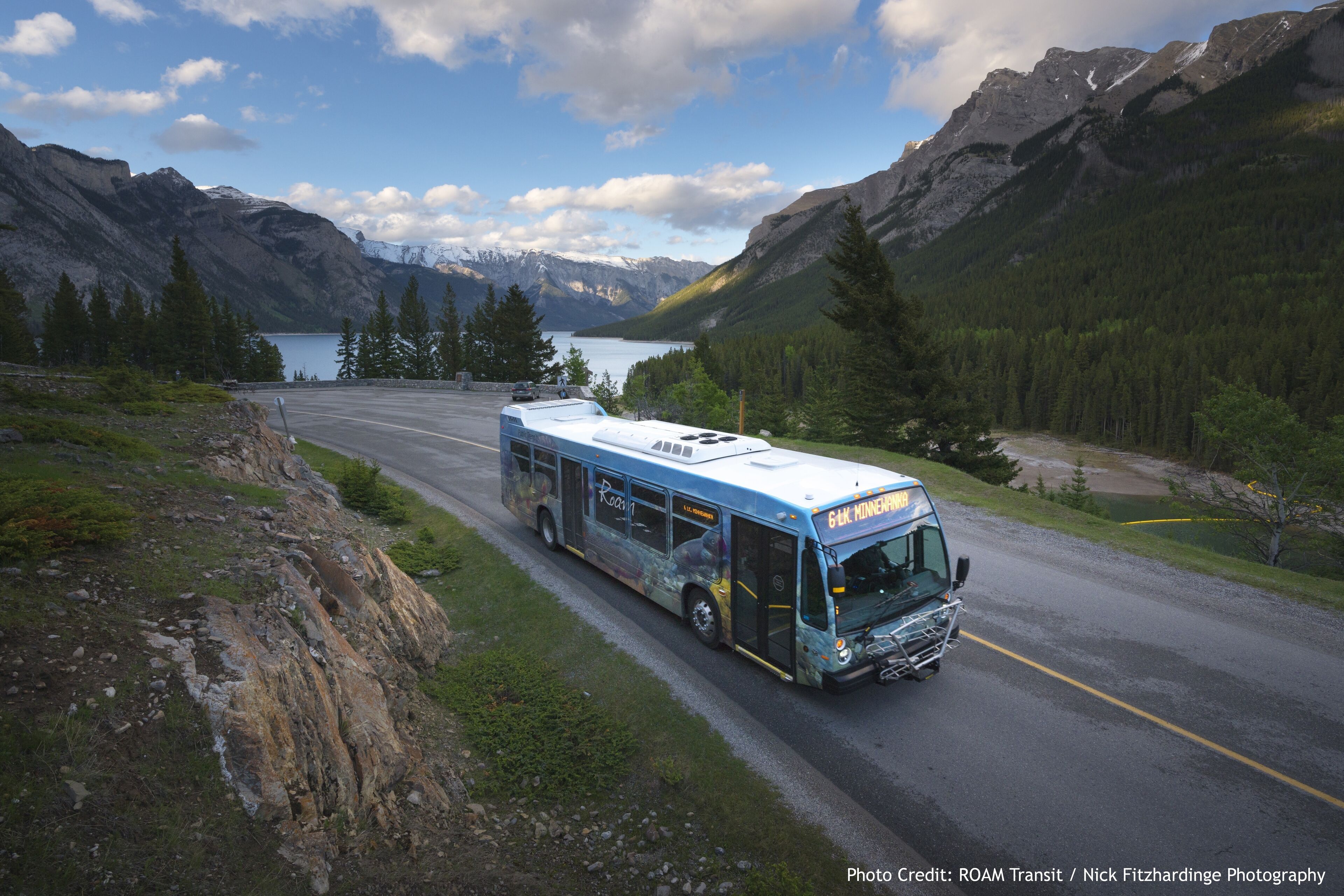 Un autobus sur une route, avec des montagnes et un lac en arrière-plan.