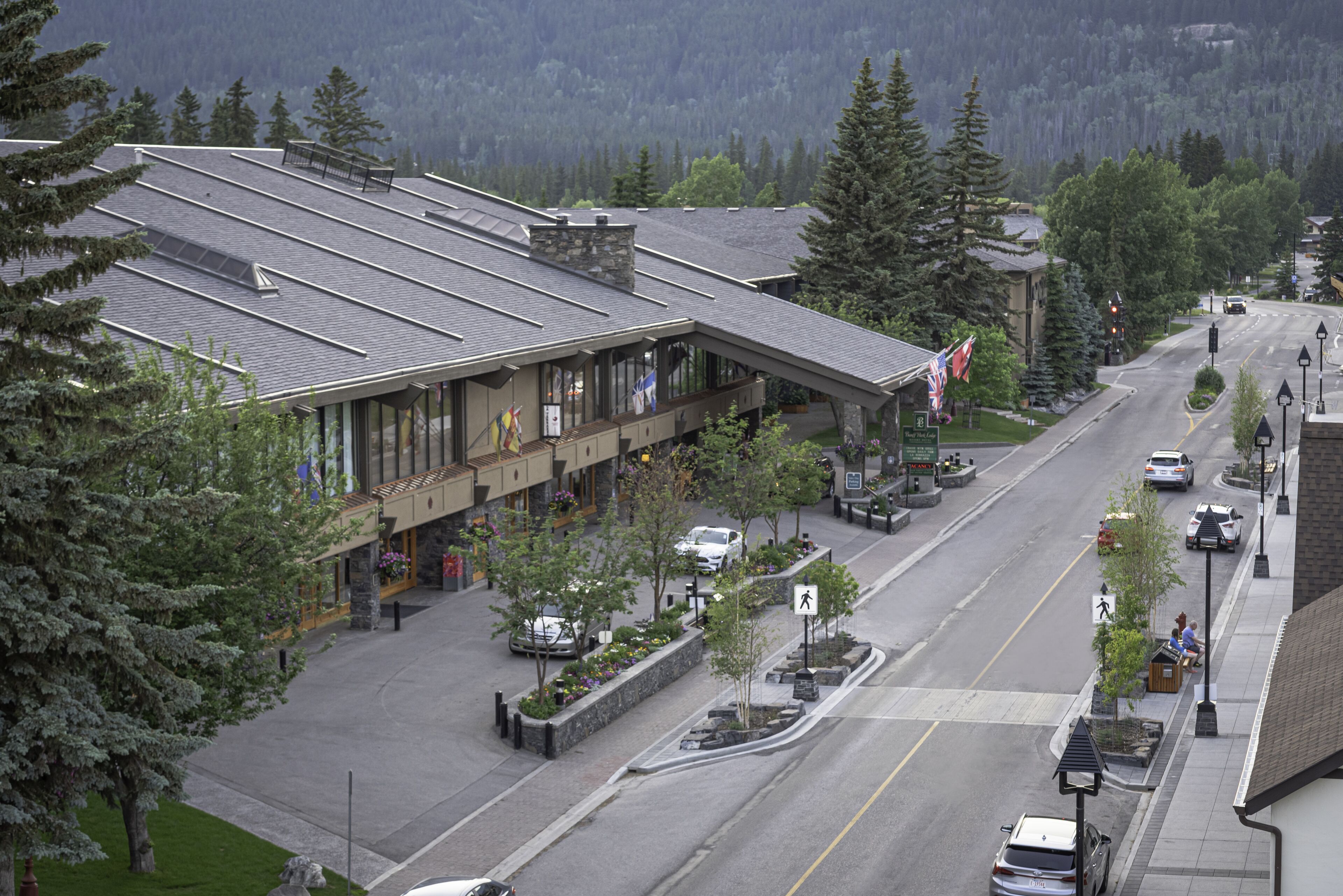 A hotel with a flat roof, large windows, and a flag. There are cars parked on the street in front.