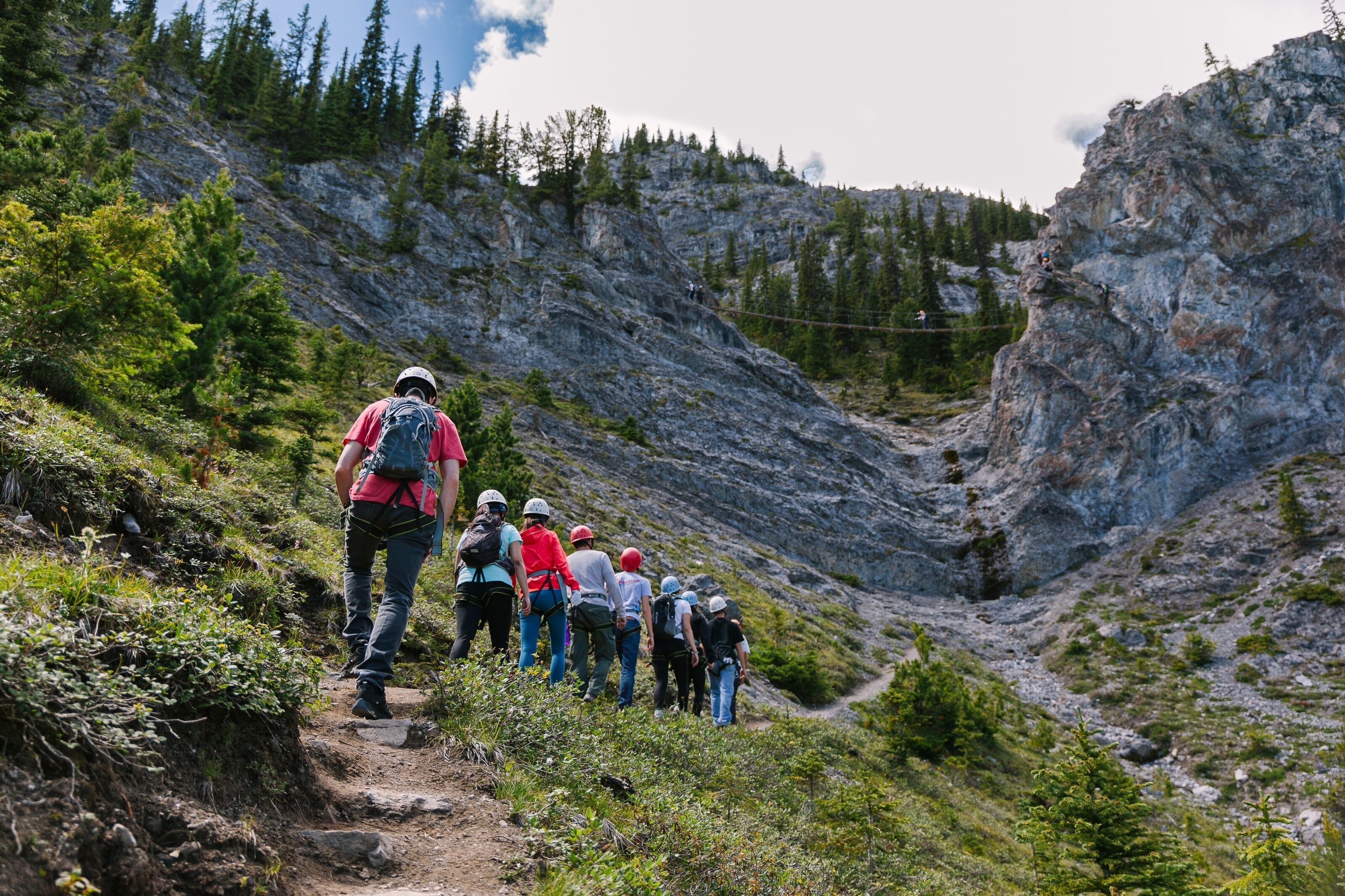 A group of hikers on a rocky trail surrounded by greenery and mountains.