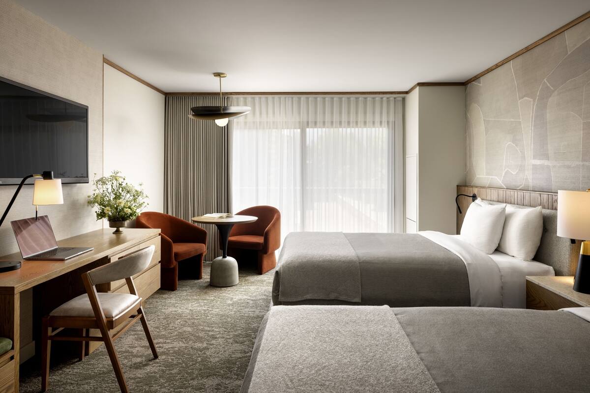 A hotel room with a bed, a desk with a laptop, a chair, a small table, and a TV.