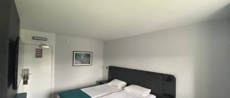 A hotel room with a bed, a nightstand, a door, and a wall-mounted picture.