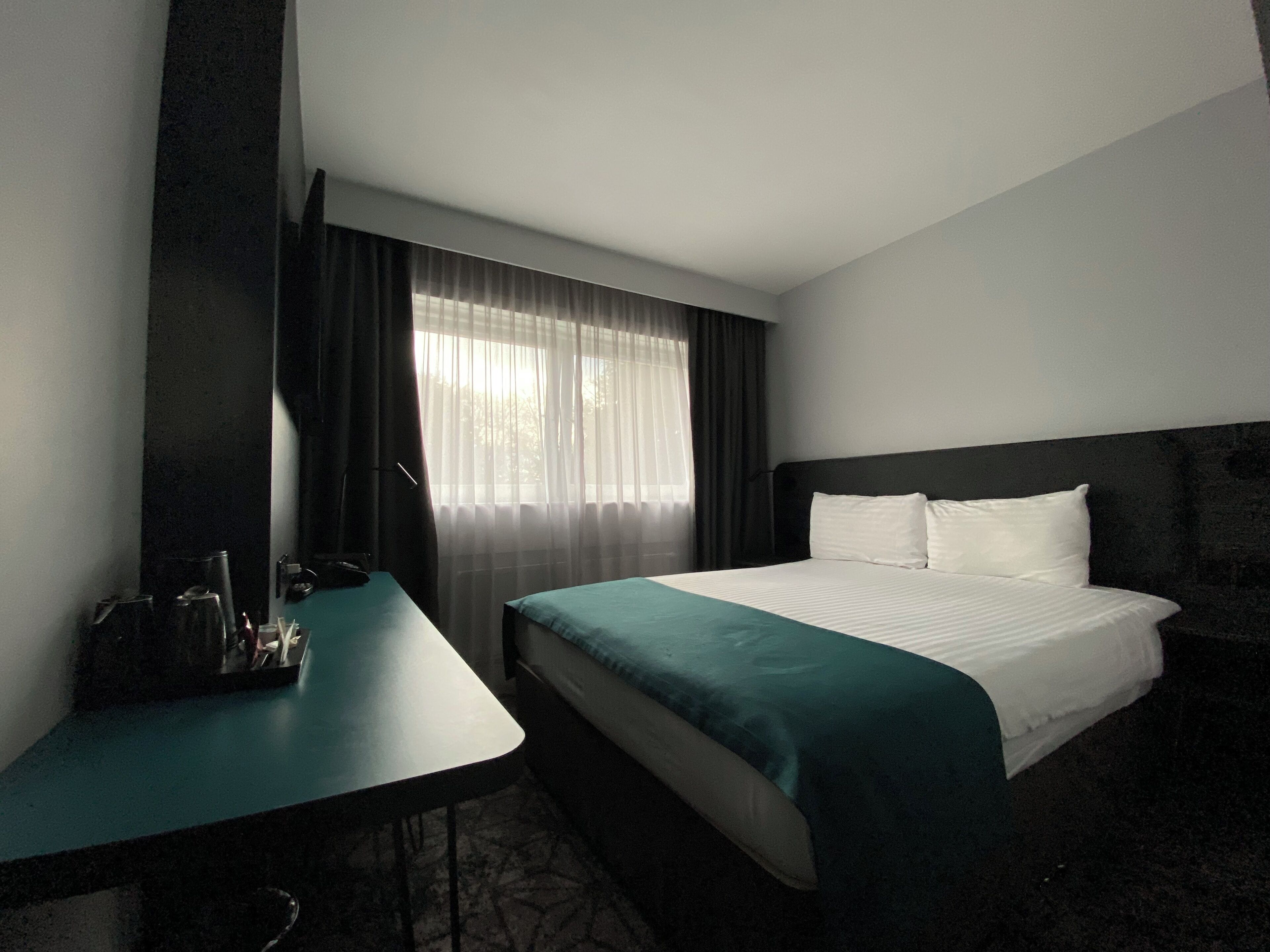 A hotel room with a bed, a desk, and a window with curtains.