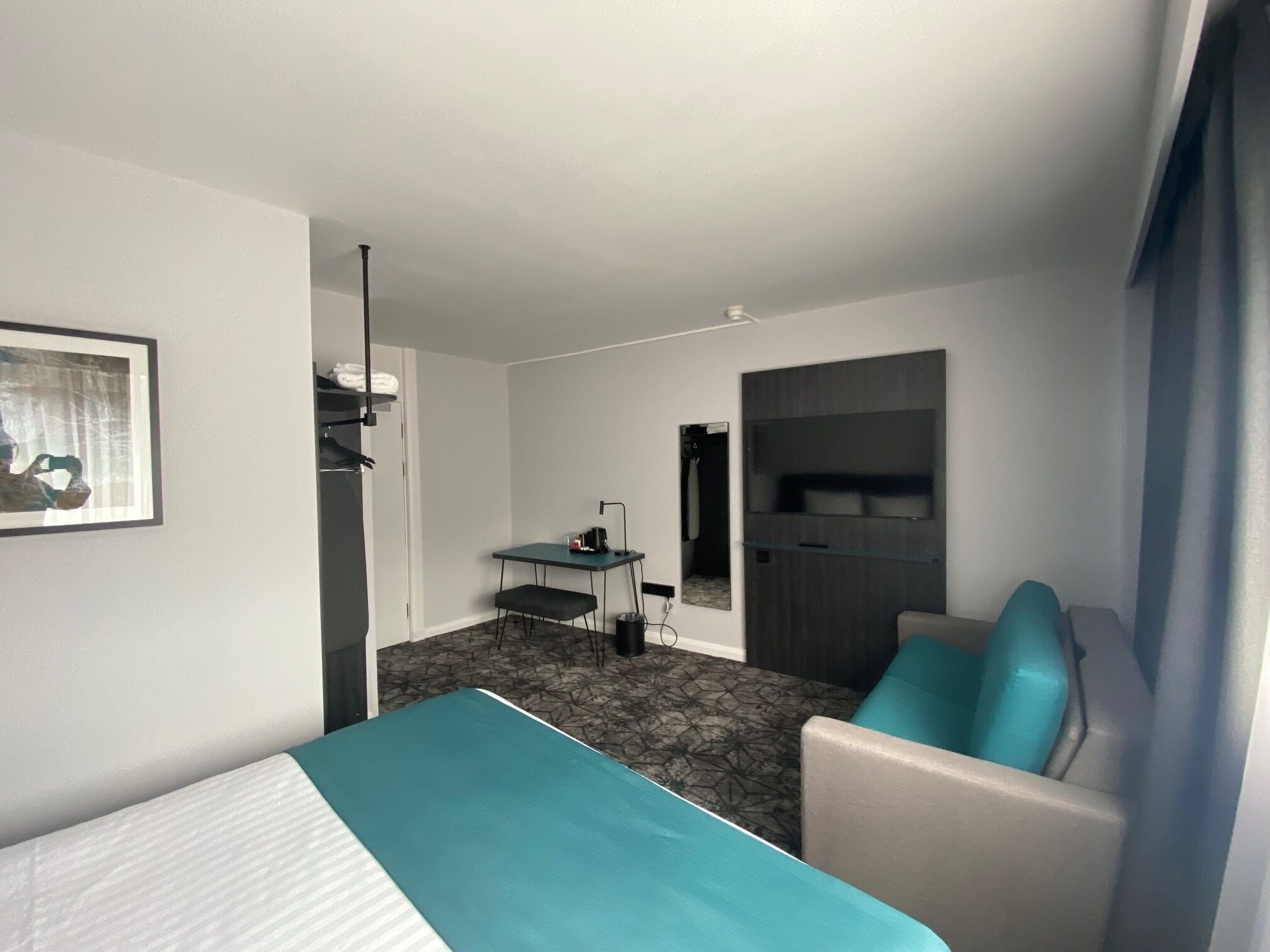 A hotel room with a bed, a desk, a chair, and a wardrobe.