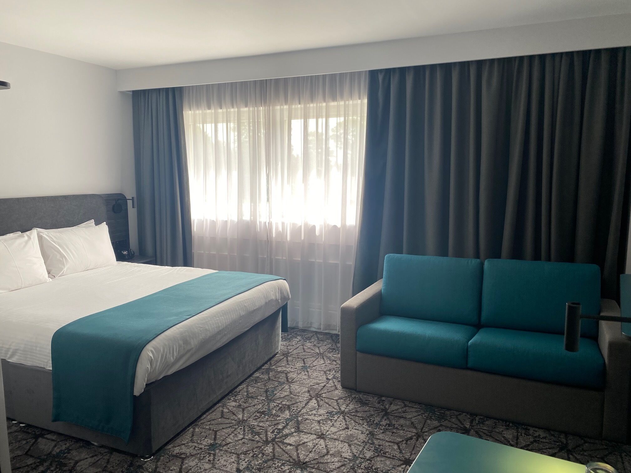 Habitació d'hotel amb un llit, un sofà i una finestra amb cortines.