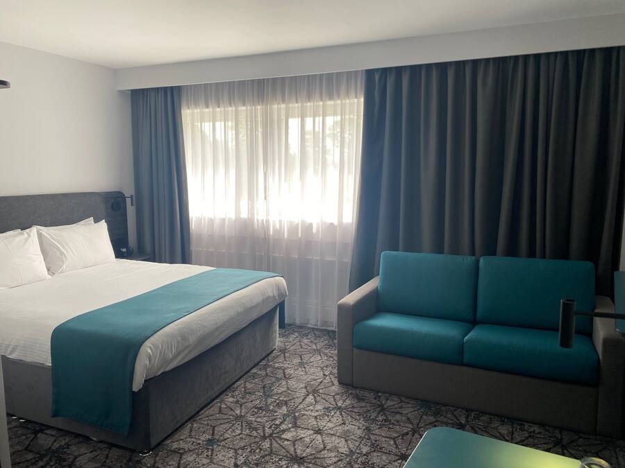 Habitació d'hotel amb un llit, un sofà i una finestra amb cortines.