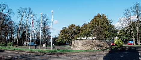 En stentavla med texten ”THE NORMANDY”, omgiven av träd och en klar himmel.