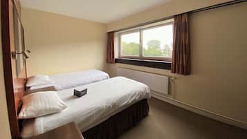 Habitación de hotel con dos camas individuales, un escritorio de madera con teléfono, una ventana con cortinas y un radiador.