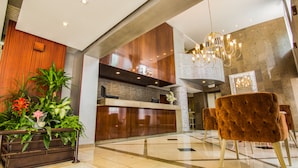 A modern lobby with a reception desk, a chandelier, and a seating area with velvet chairs. - GHL Hotel Hamilton (Bogotá)