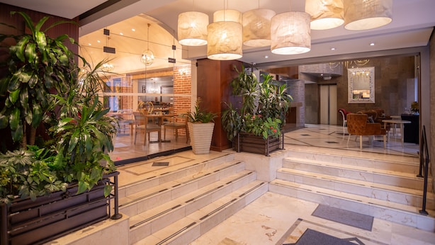 A hotel lobby with a staircase, large potted plants, and a seating area. - GHL Hotel Hamilton (Bogotá)