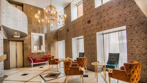 A spacious lobby with a high ceiling, a chandelier, patterned walls, and a mix of seating options including red sofas and orange chairs. - GHL Hotel Hamilton (Bogotá)