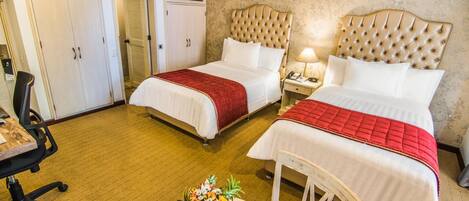 A hotel room with two beds, a desk, a chair, and a table with a floral arrangement.