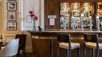 A bar area with a marble counter, two bar stools, a vase with red flowers, and a wall with framed pictures.
