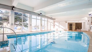 An indoor swimming pool with clear glass walls, a tiled floor, and a metal ladder.