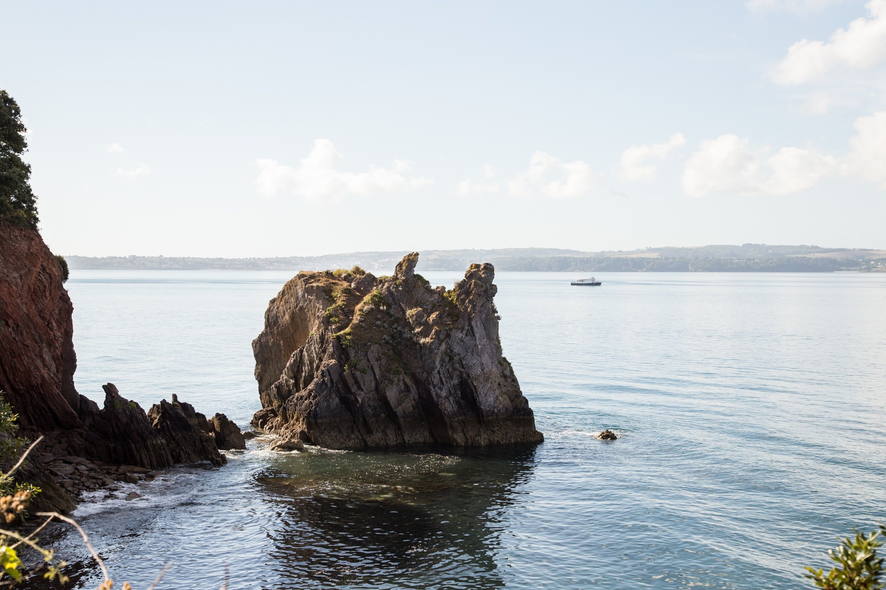 A coastal landscape with a prominent rock formation and calm sea.