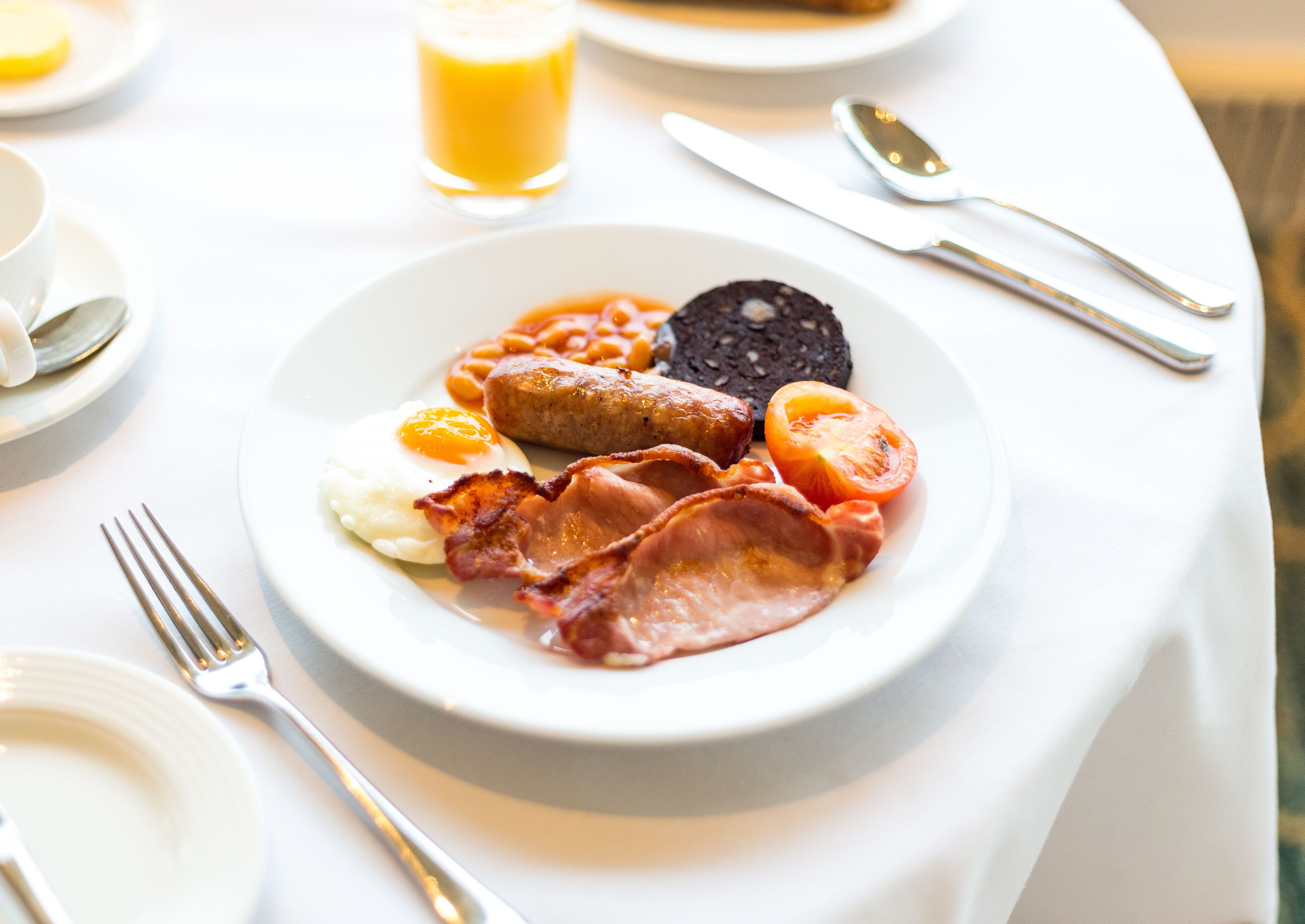 A breakfast plate with eggs, bacon, sausages, beans, and a slice of black pudding.