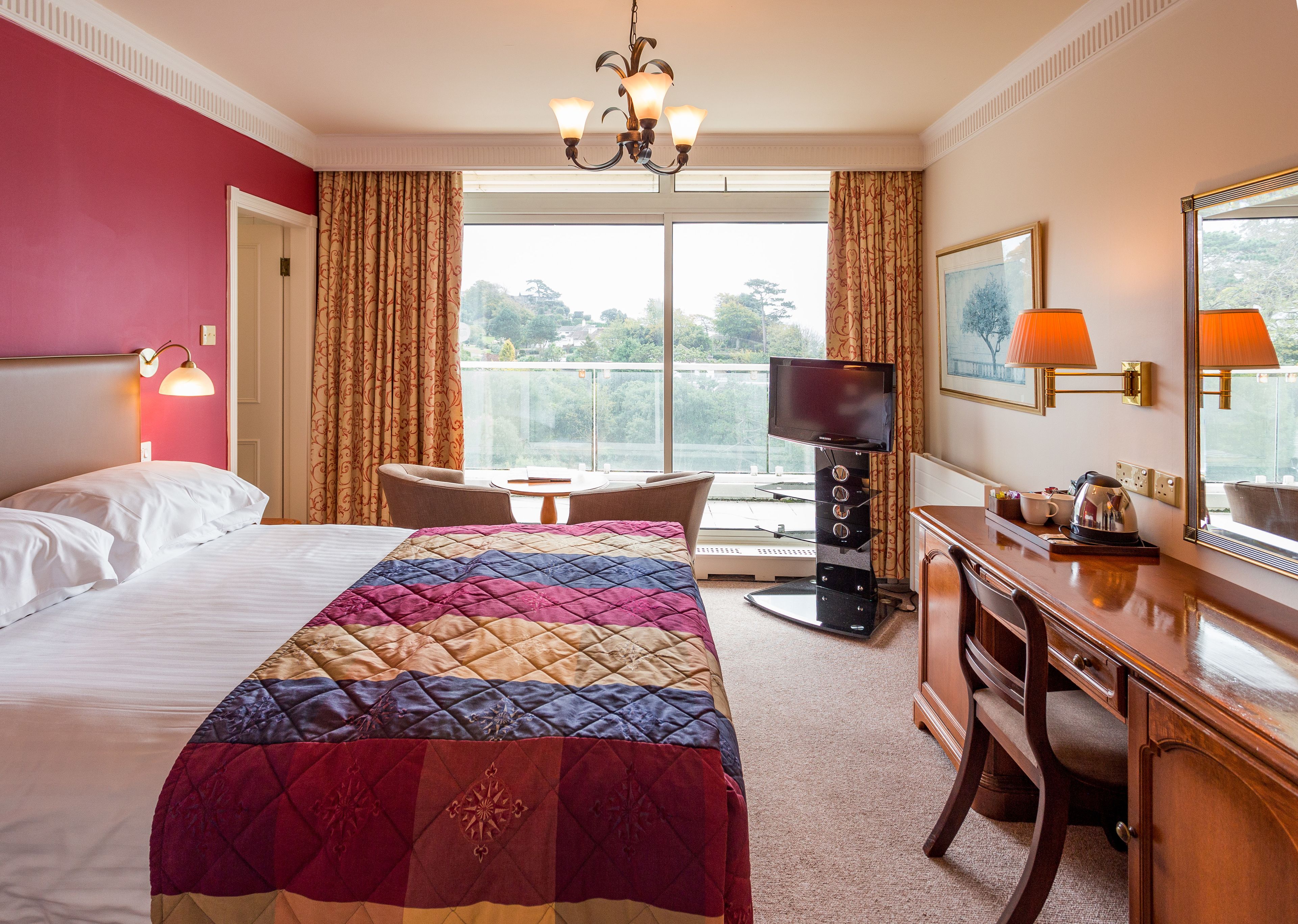A hotel room with a large bed, a desk with a chair, a television, and a view of the outdoors.