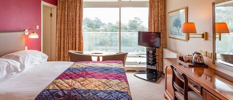 A hotel room with a large bed, a desk with a chair, a television, and a view of the outdoors.