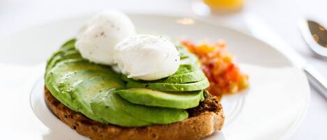 Un plato de desayuno con tostadas de aguacate, huevos pochados y una guarnición de verduras.