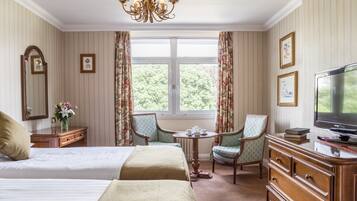 A hotel room with two beds, a television, a dresser, a chair, and a window with a view of trees.
