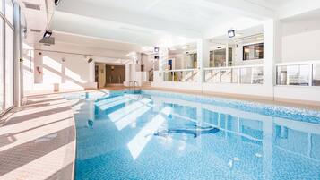 A large indoor swimming pool with clear blue water, surrounded by white walls and a tiled floor.