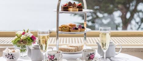 Un présentoir à trois niveaux, garni de diverses pâtisseries, et une théière, le tout posé sur une table avec des tasses à thé et une coupe de champagne.