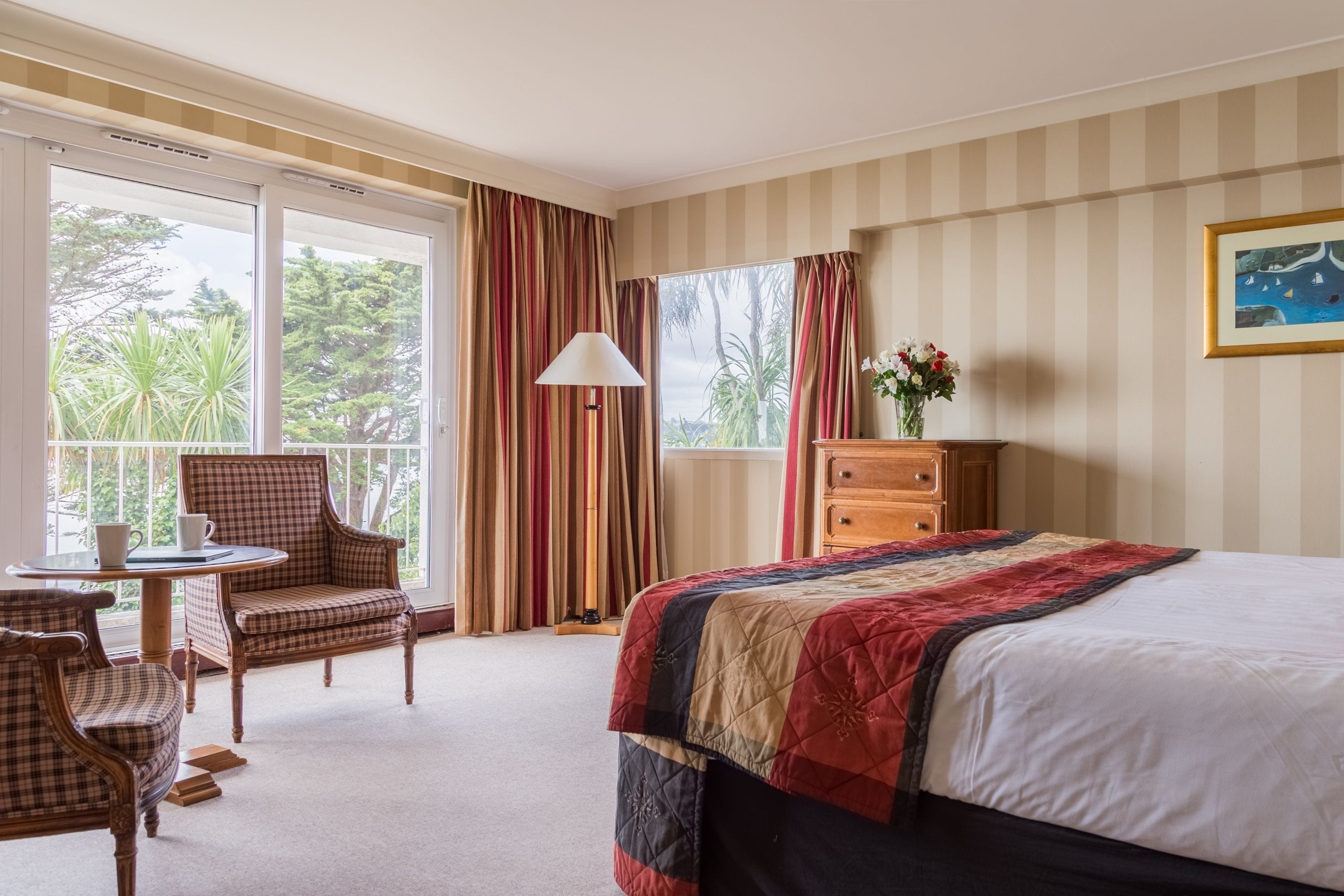 A hotel room with a large bed, a desk with a chair, a dresser, and a window with curtains.
