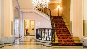 A grand staircase with a red carpet, a chandelier, and a lamp.
