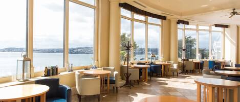 A spacious indoor area with large windows offering a view of a body of water and distant landscape.