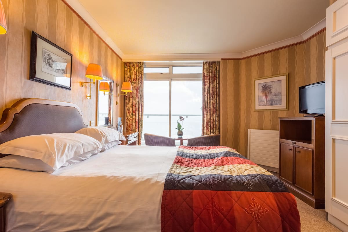 Habitación de hotel con una cama grande, un escritorio, una silla, un televisor y una ventana con cortinas.