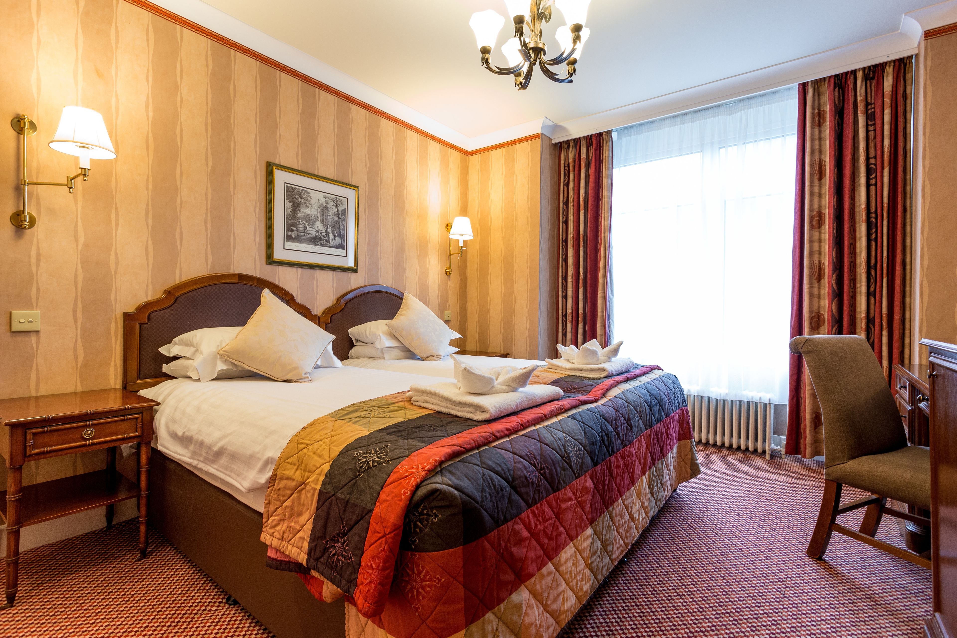 Una habitación de hotel con una cama grande, dos mesitas de noche, una silla y un candelabro.
