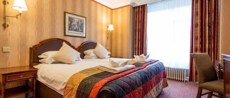 A hotel room with a large bed, two bedside tables, a chair, and a chandelier.