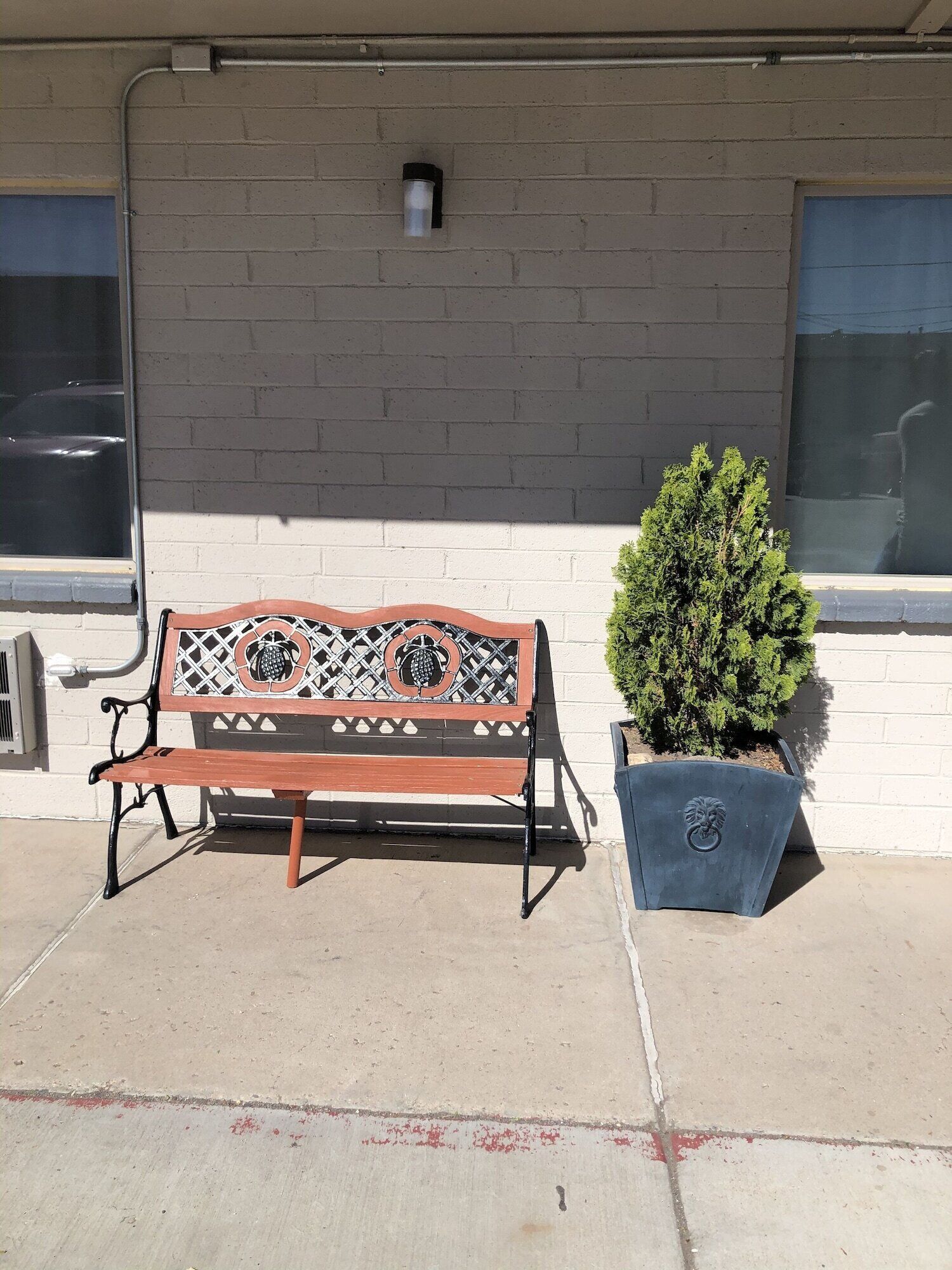 A bench with a decorative backrest and a potted plant beside a building with a brick wall and windows.