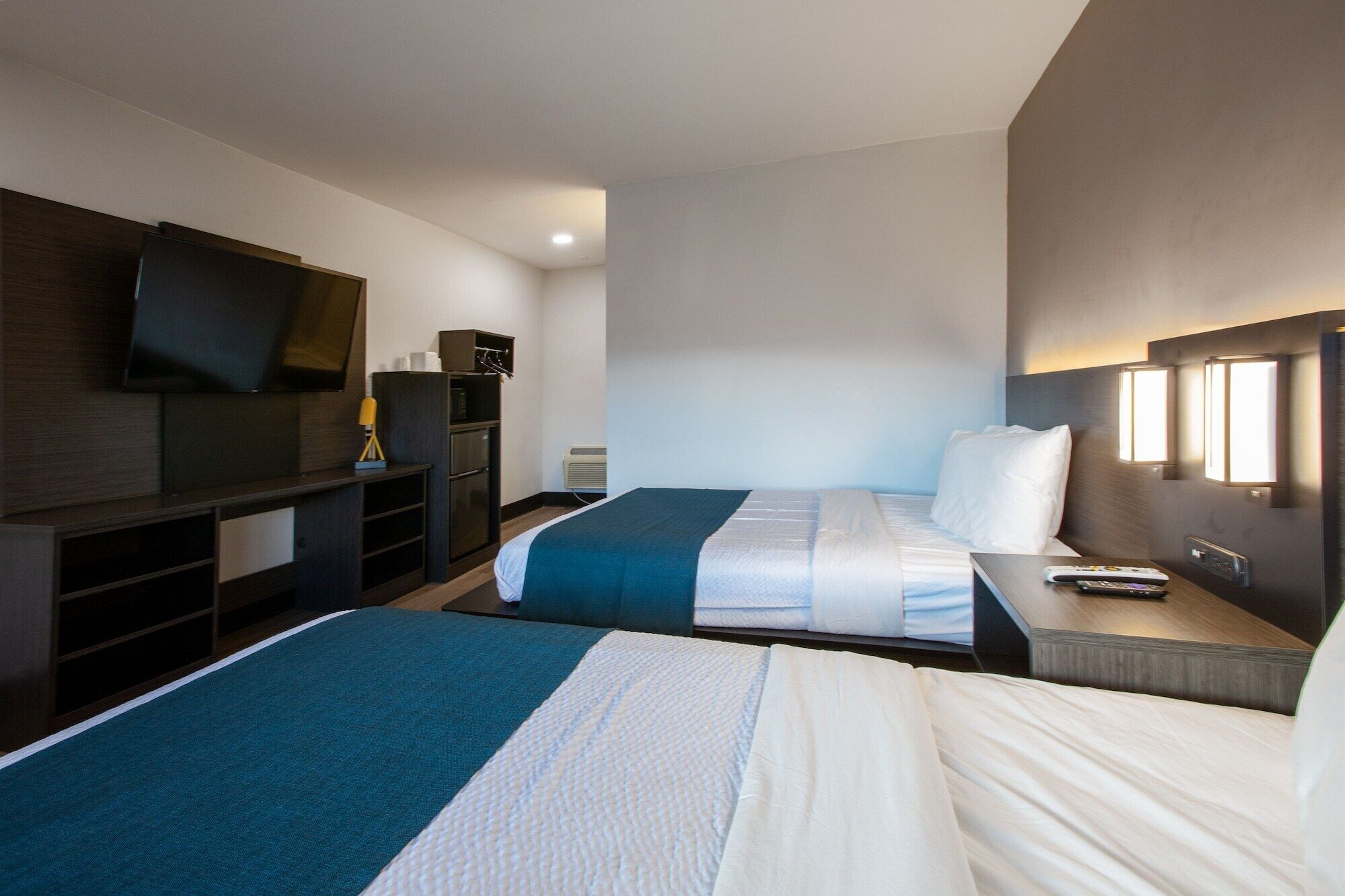 Une chambre d’hôtel avec deux lits, une télévision, un bureau, une lampe et un luminaire fixé au mur.